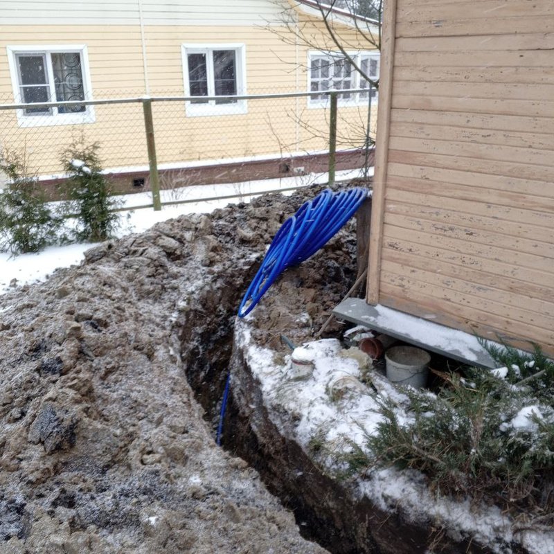 Водопроводная труба в траншее у фундамента дома зимой